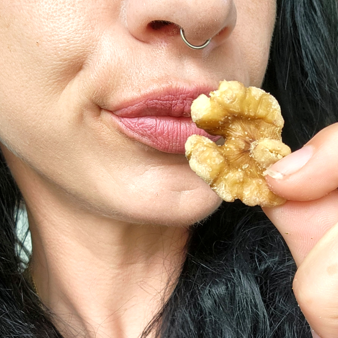 Close-up of a person holding a cracked walnut near their mouth.